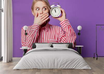 Beautiful woman in red striped shirt with alarm clock on purple background Wall mural