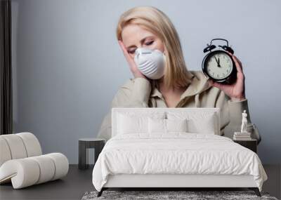 Blonde woman in protective mask with alarm clock on grey background Wall mural