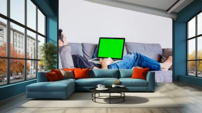 Man lying down on sofa with laptop computer Wall mural