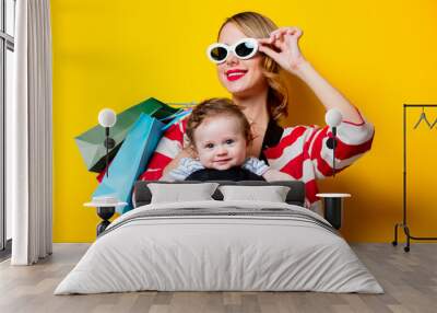 Mother and little baby in carrier have a shopping with bags. Models on yellow background Wall mural