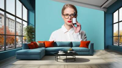 Portrait of beautiful blonde in white shirt with cosmetic bottle on blue background Wall mural