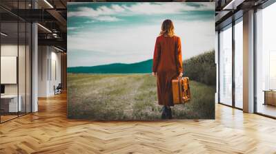 Portrait of young woman in red coar at autumn countryside with suitcase. Wall mural