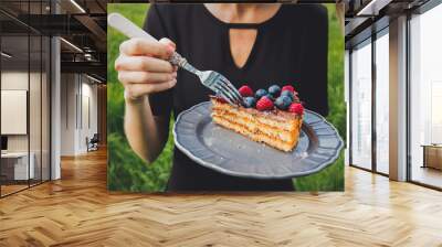 Woman eating a chocolate covered blueberry and raspberry pice of cake on outdoor Wall mural