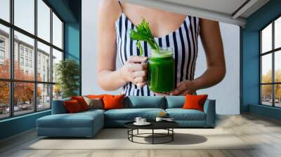 Woman holding a glass with celery juice Wall mural