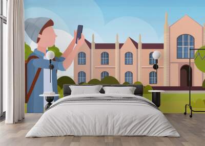 man taking selfie photo on smartphone camera casual male cartoon character in hat with backpack over university building exterior flat portrait horizontal Wall mural