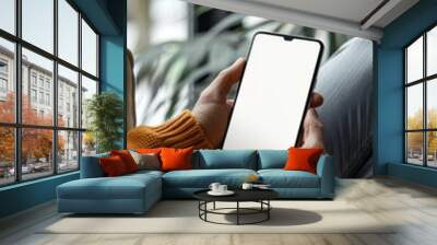 Mockup image of mobile smartphone with blank screen template, man sitting on sofa, hand holding and looking at mobile phone screen  Wall mural