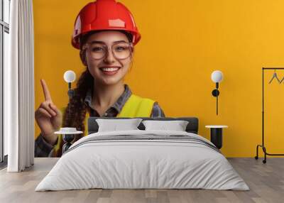 young woman in construction uniform and red safety helmet smiling and pointing with finger Wall mural