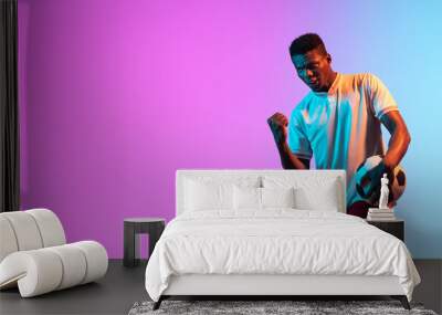 African man, professional football player standing isolated on gradient blue pink background in neon light. Wall mural