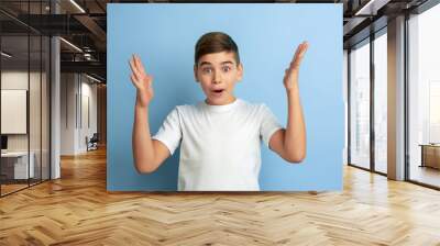 Astonished, shocked, wondered. Caucasian boy portrait isolated on blue studio background. Beautiful teen male model in white shirt posing. Concept of human emotions, facial expression, sales, ad. Wall mural