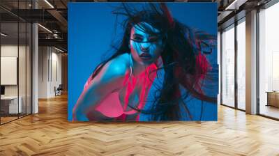 Attractive brunette model on blue studio background in neon light. Beautiful women in underwear posing with flying hair and dark make up. Concept of sensuality, style, fashion industry, characters. Wall mural