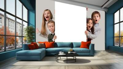 Banner with a surprised children peeking at the edge with copyspace. The portrait of cute little kids boy and girls looking at camera against white studio wall. Kids fashion and happy emotions concept Wall mural