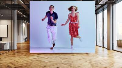 Beautiful girl and man in colorful costumes dancing retro style dances against gradient blue purple studio background. Concept of art, retro style, hobby, party, fun, movements, 60s, 70s culture Wall mural