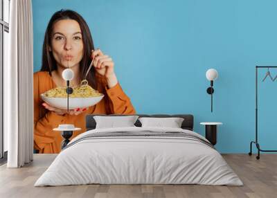 Beautiful young girl eating delicious Italian pasta isolated on blue studio background. World pasta day Wall mural