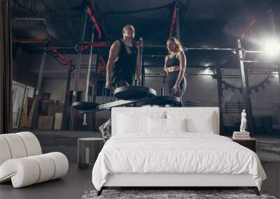 Beautiful young sporty couple workout in gym together. Caucasian man training with female trainer. Concept of sport, activity, healthy lifestyle, strength and power. Working out sit ups with weights. Wall mural