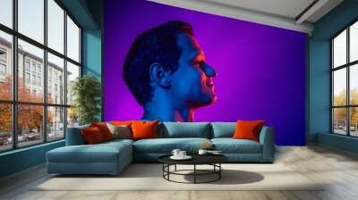 Caucasian man's portrait on purple blue studio background in multicolored neon light. Beautiful male model. Concept of human emotions, facial expression, sales, ad, fashion. Copyspace. Wall mural