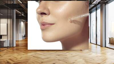 Close up beautiful young woman applying serum, oil on face on white background. Concept of cosmetics, makeup, natural and eco treatment, skin care. Shiny and healthy skin, fashion, healthcare. Wall mural