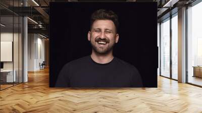 Close up portrait of young man isolated on black studio background. Photoshot of real emotions of male model. Smiling, feeling crazy happy, laughting. Facial expression, human emotions concept. Wall mural