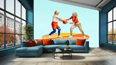 Competition. Two middle-aged, senior women in stylish sportswear playing with basketball ball against light blue background. Concept of sportive lifestyle, health, action and motion. Copy space for ad Wall mural