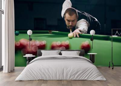 Concentrated young man leaning on billiards table, playing snooker game. Lifestyle magazine spread highlighting leisure activities. Concept of billiards sport, gambling, hobby, leisure, game Wall mural