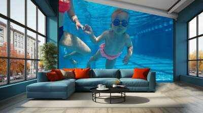 Cute, funny, little baby girl, toddler in goggles swimming underwater in swimming pool with instructor. Water sports activity. Concept of sport, healthy and active lifestyle, childhood, fun, training Wall mural