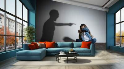 Domestic violence, abusing. Scared little caucasian girl, victim sitting close to white wall with shadow of angry father's threatening on it. Awareness of social problem, childhood, physical violence. Wall mural