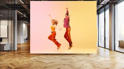 Dynamic image of beautiful young couple, man and woman in stylish vintage clothes dancing against gradient pink yellow background. Concept of retro style, dance, fashion, art, hobby, music, 70s Wall mural