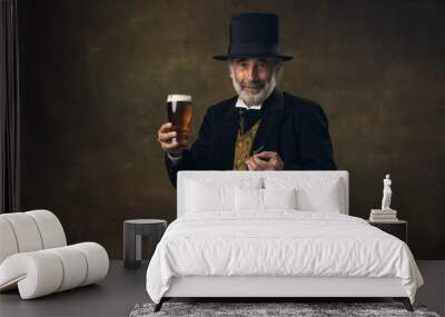 Elderly gray-haired man, gentleman, aristocrat or actor drinking beer isolated on dark vintage background. Retro style, comparison of eras concept. Wall mural