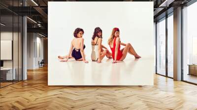 Elegant, beautiful young girls in stylish vintage swimsuit sitting and looking back against white background. Retro sport, cruise. Concept of summer vacation, travelling, retro style, fashion Wall mural