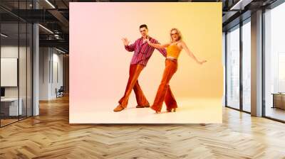 Expressive, talented, emotional couple, man and woman in stylish clothes dancing disco dance against gradient pink yellow background. Concept of retro style, dance, fashion, art, hobby, music, 70s Wall mural