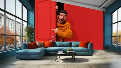 Extremely happy man with moustaches peeking out red door and pointing with positive excitement. Sales, job fair, betting, win, success. Concept of emotions, facial expression, lifestyle Wall mural