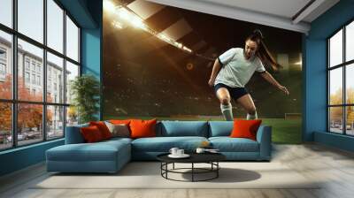 Female soccer, football player dribbling ball in motion at stadium during sport match over evening sky background. Wall mural