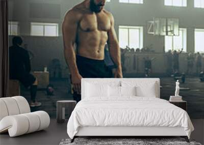 Fit young man lifting barbells working out in a gym Wall mural