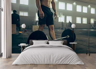 Fit young man lifting barbells working out in a gym Wall mural