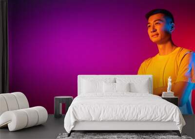 Flyer. Asian young man isolated on studio background in gradient pink purple neon light, colour filter. Concept of human emotions, facial expression. Wall mural