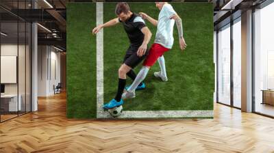 Football player tackling for ball over green grass background. Professional male soccer players in motion at stadium. Fit jumping men in action, jump, movement at game. Wall mural