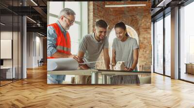 Foreman or achitect engineer shows future house, office or store design plans and model to a young couple. Meeting at the construction office to talk about facade, interior decoration, home layout. Wall mural