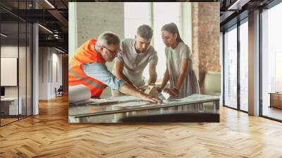 Foreman or achitect engineer shows future house, office or store design plans and model to a young couple. Meeting at the construction office to talk about facade, interior decoration, home layout. Wall mural