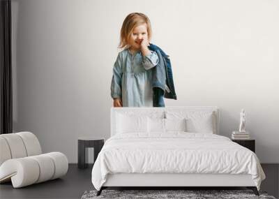 Full length portrait of cute little kid girl in stylish jeans clothes looking at camera and smiling, standing against white studio wall. Kids fashion concept Wall mural