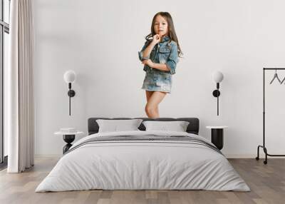 Full length portrait of cute little kid girl in stylish jeans clothes looking at camera and smiling, standing against white studio wall. Kids fashion concept Wall mural