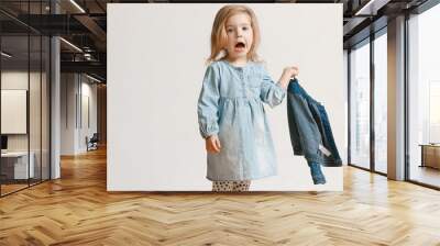 Full length portrait of cute little kid girl in stylish jeans clothes looking at camera and smiling, standing against white studio wall. Kids fashion concept Wall mural