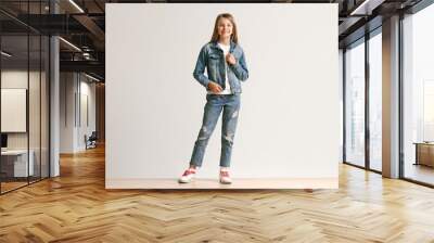 Full length portrait of cute little teen girl in stylish jeans clothes looking at camera and smiling against white studio wall. Kids fashion concept Wall mural