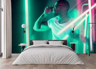 Geometric lines. Cinematic portrait of stylish young man in neon lighted room. Bright neoned colors. African-american model, musician indoors. Youth culture in party, festival style and music concept. Wall mural