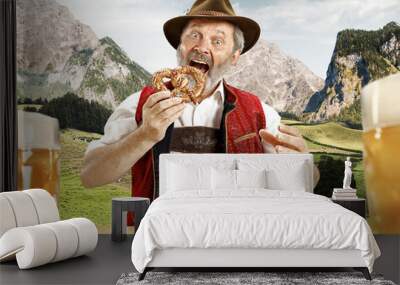 Germany, Bavaria. The senior happy smiling man with beer dressed in traditional Austrian or Bavarian costume with Bavarian pretzels against Alpine mountain landscape. oktoberfest, festival concept Wall mural