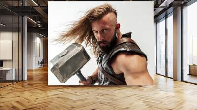 God of thunder. Blonde long hair and muscular male model in leather viking's costume with the big hammer cosplaying Thor isolated on white studio background. Fantasy warrior, antique battle concept. Wall mural