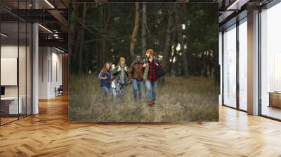 Group of friends on a camping or hiking trip in autumn day. Men and women with touristic backpacks going throught the forest, talking, laughting. Leisure activity, friendship, weekend. Wall mural