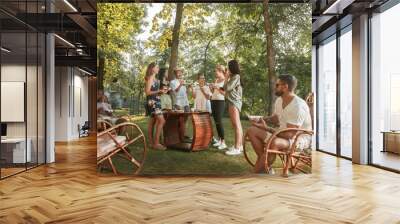 Group of happy friends eating and drinking beers at barbecue dinner on sunset time. Having meal together outdoor in a forest glade. Celebrating and relaxing. Summer lifestyle, food, friendship concept Wall mural