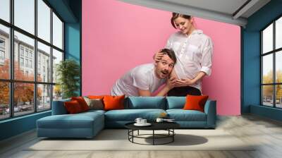 Handsome man is listening to his beautiful pregnant wife's tummy and smiling Wall mural