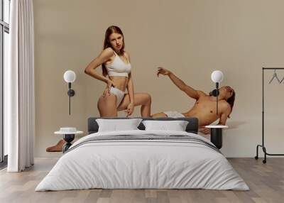 Handsome shirtless man and elegant young girl posing in underwear against warm grey background. Models showing athletic bodies. Concept of beauty, body, sport and health, fashion Wall mural