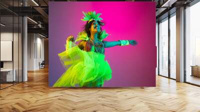 Happiness. Beautiful young woman in carnival, stylish masquerade costume with feathers dancing on gradient background in neon light. Concept of holidays celebration, festive, dance, party, having fun. Wall mural