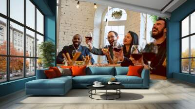 Happy co-workers celebrating while company party, corporate event. Young caucasian people in business attire talking, drinking wine. Concept of office culture, teamwork, friendship, holidays, weekend. Wall mural